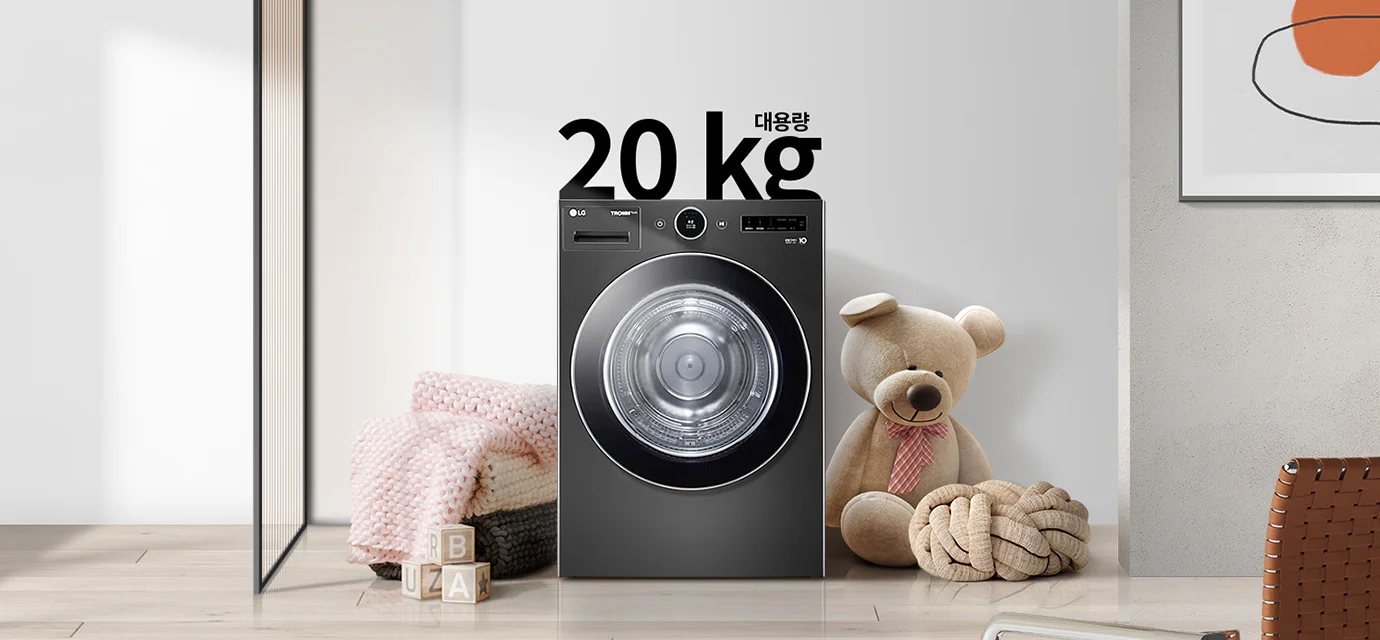 검정색 세탁기가 있으며, 상단에 20kg 대용량이라는 문구가 있습니다. 세탁기 옆에는 곰 인형과 두꺼운 니트 담요가 놓여 있고, 바닥에는 알파벳 블록이 있습니다. 