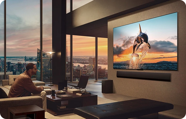 도시 풍경을 감상할 수 있는 넓은 거실. LG OLED TV는 LG 사운드바가 있는 벽에 장착되어 있습니다. TV의 원월 디자인으로 벽에 플러시 핏을 맞추고 공간과 잘 어우러집니다. 제로 커넥트 박스는 보이지만 숨겨져 있습니다.