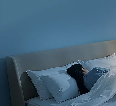 침대에 누워 있는 사람이 하얀 베개와 이불을 덮고 잠들어 있는 모습입니다. 벽은 부드러운 파란색으로 칠해져 있으며, 방 안은 차분하고 조용한 분위기를 자아내고 있습니다.