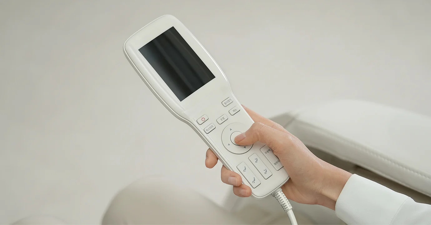 손이 흰색 리모컨을 잡고 있으며, 리모컨에는 작은 화면과 여러 개의 버튼이 있습니다. 버튼에는 전원, 온도, 모니터, 원상복귀, 메뉴, 무중력, 무중력 해제 등의 텍스트가 적혀 있습니다. 배경은 밝은 색상으로 되어 있습니다.