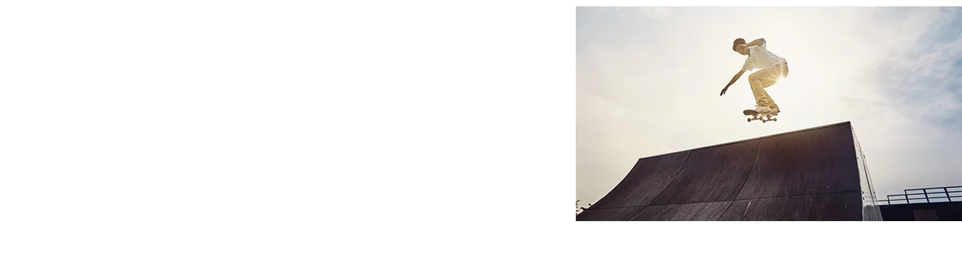스케이트보드를 타는 사람이 램프에서 공중으로 점프하고 있습니다. 하늘은 맑고 햇빛이 비치고 있으며, 주변은 스케이트파크의 구조물로 보입니다.